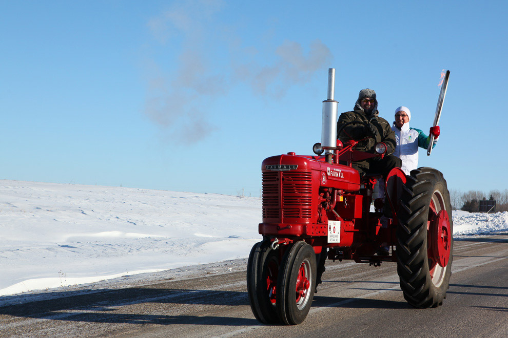 Джон Нельсон едет на старом тракторе, держа факел с олимпийским огнем, в Нипаве, Канада, 8 января 2010 г. (© VANOC / COVAN)