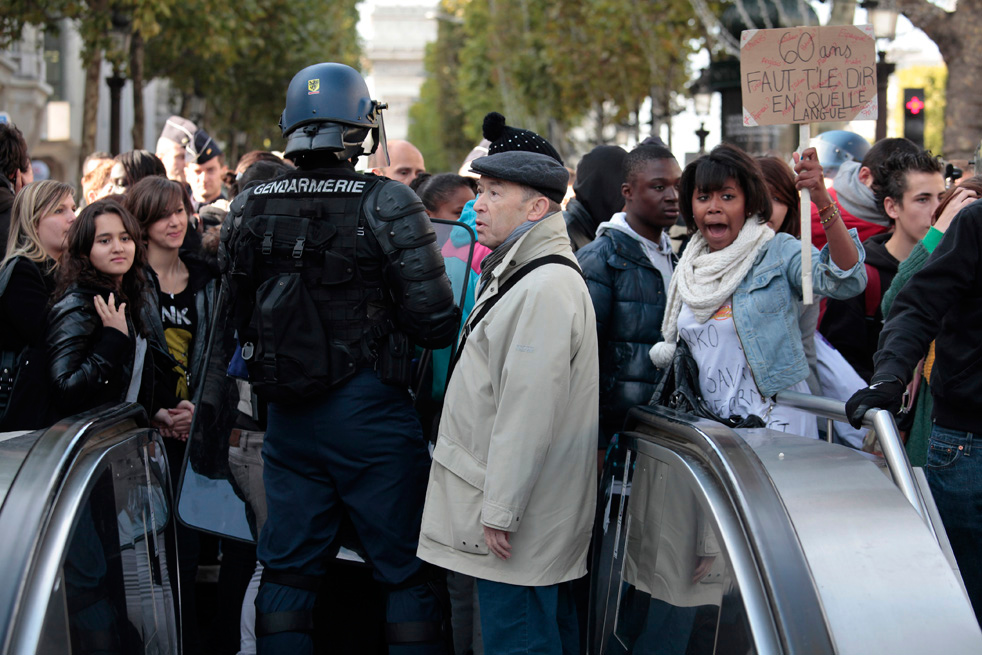 Прохожие смотрят на митингующих студентов, скандирующих лозунги на Елисейских полях в Париже 18 октября 2010 года. (AP / Thibault Camus)