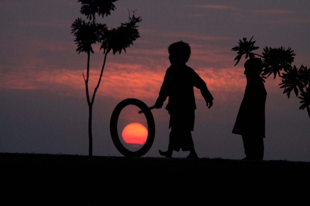 Дети играют с колесом на фоне заката.