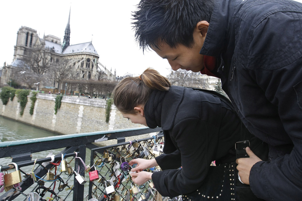 Парень и девушка вешают замок на ограду моста.