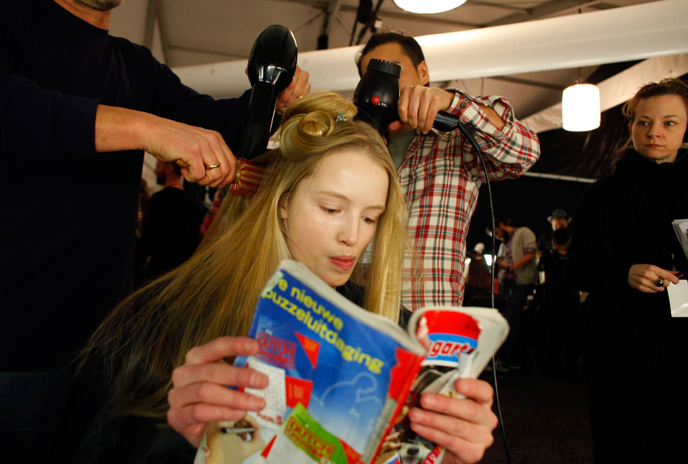 Парикмахеры причёсывают девушку, читающую журнал.