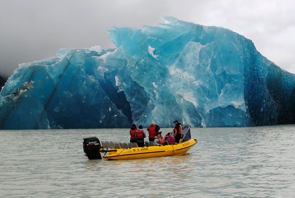 Люди плывут в лодке около айсберга.
