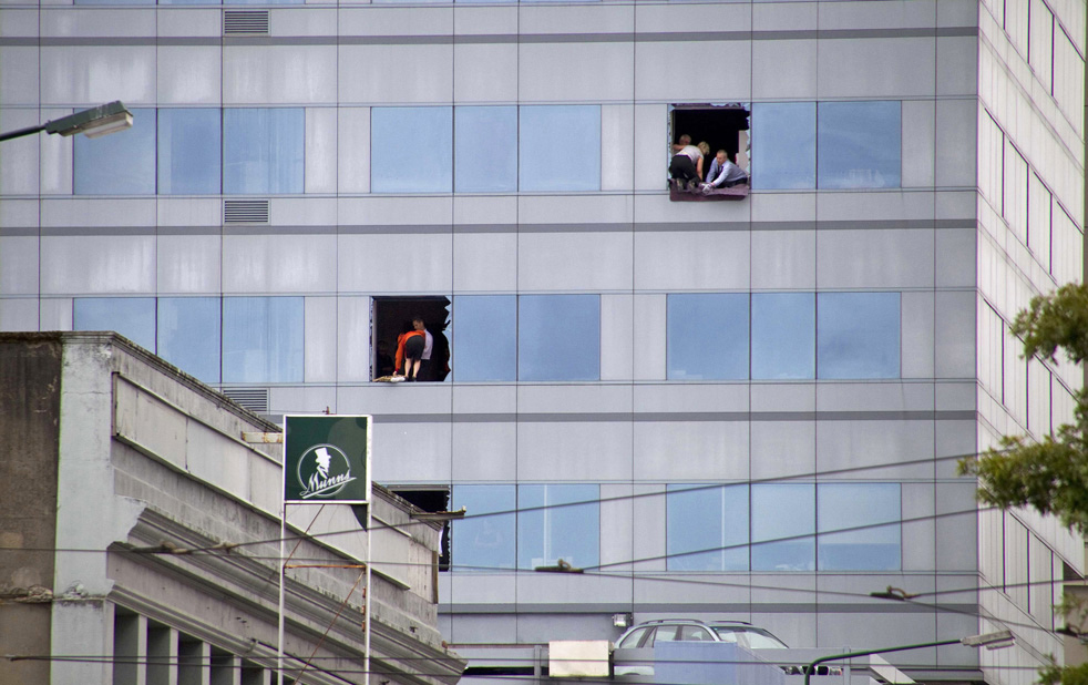 Люди высовываются в разбитые окна высотного здания.