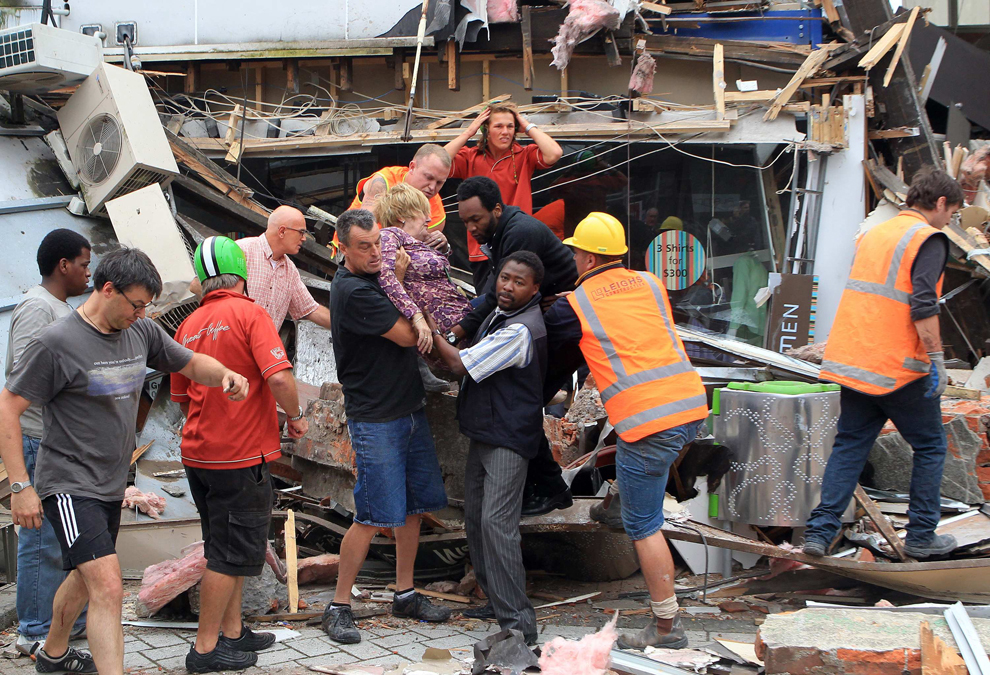 Спасатели вытаскивают женщину из разрушенного здания.