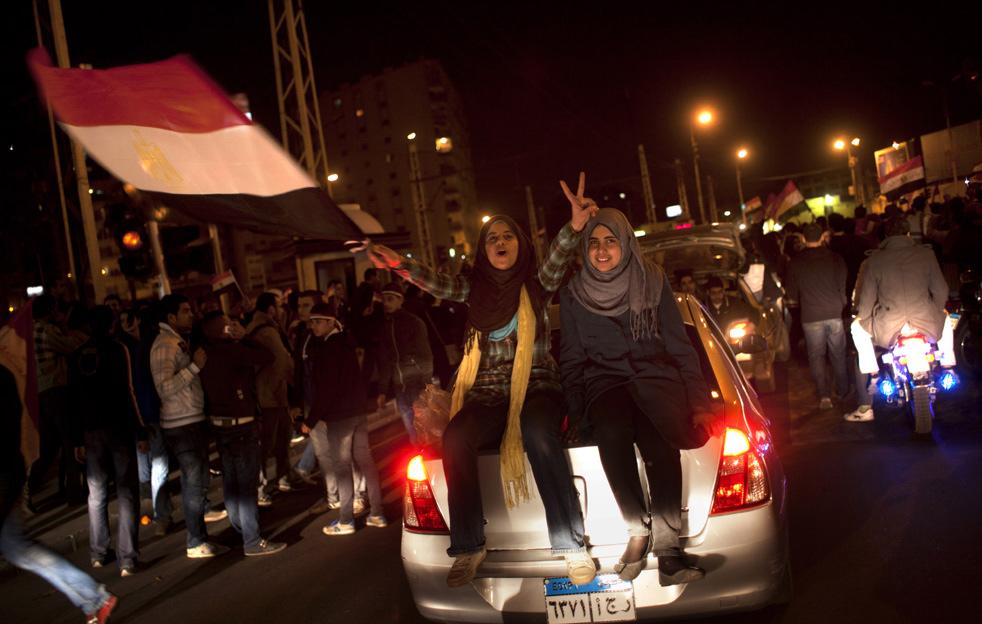 Девушки сидят на автомобиле и показывают знак победы.