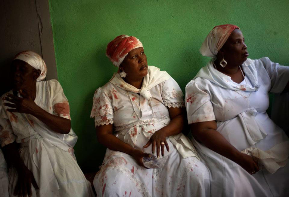 Женщины в одежде, запятнанной кровью жертвенного животного, убитого прошлым воскресеньем во время церемонии Вуду в Сувеннасе, Гаити.