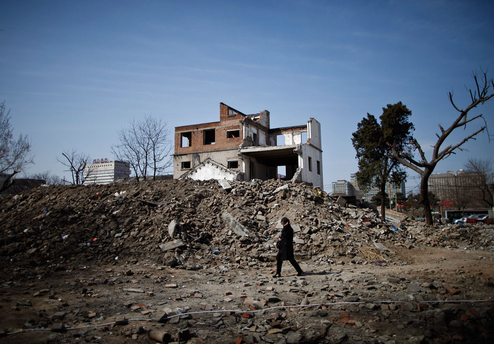 Женщина проходит мимо частично разрушенных зданий
