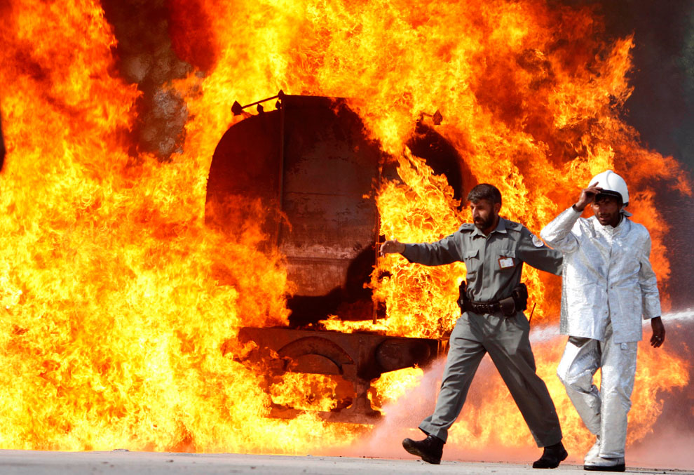 Афганский полицейский уводит пожарного от горящей цистерны