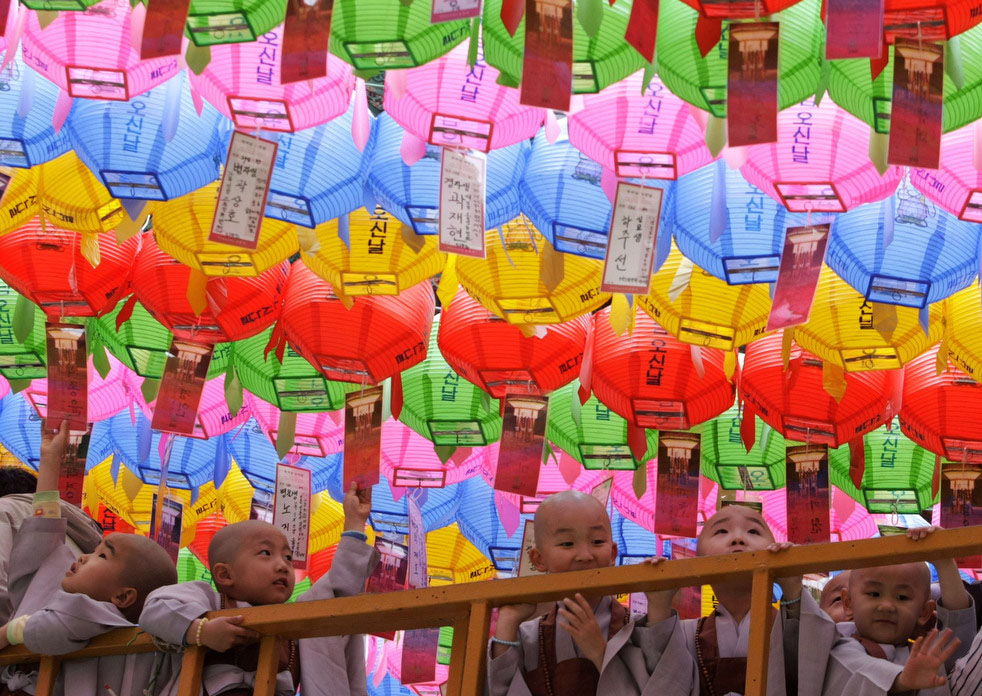 Юные монахи стоят под разноцветными фонариками