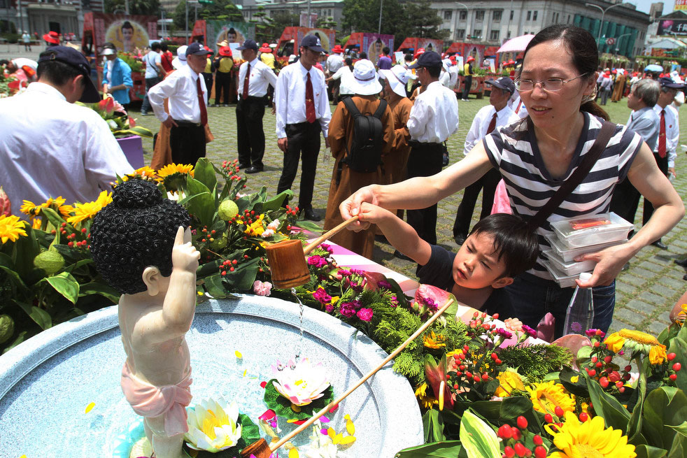 Мать помогает своему ребёнку омыть статую маленького Будды