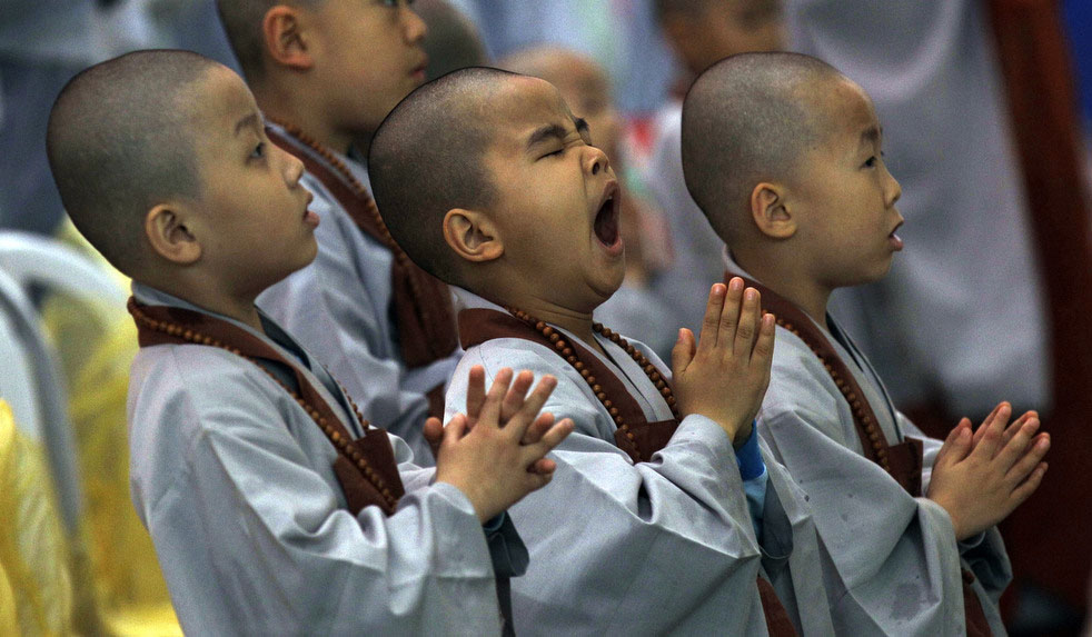 Бритоголовый мальчик-буддист зевает во время службы