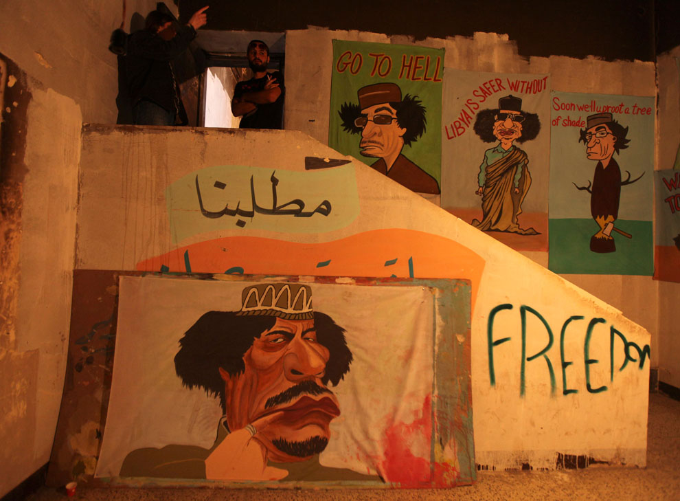 Люди стоят рядом с карикатурными изображениями Муаммара Кадафи
