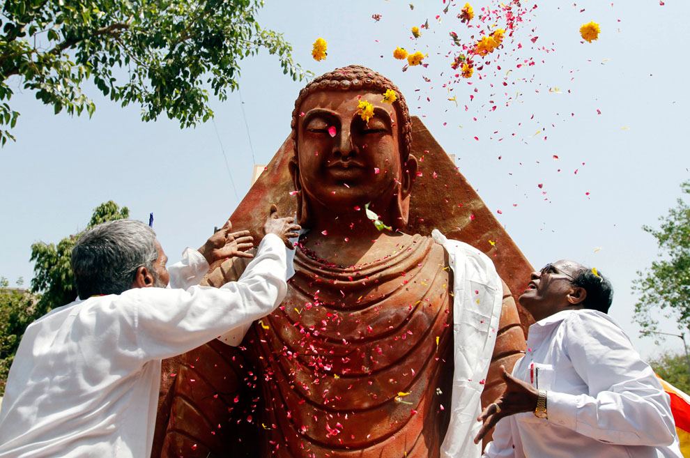 Верующие осыпают лепестками цветов статую сидящего Будды