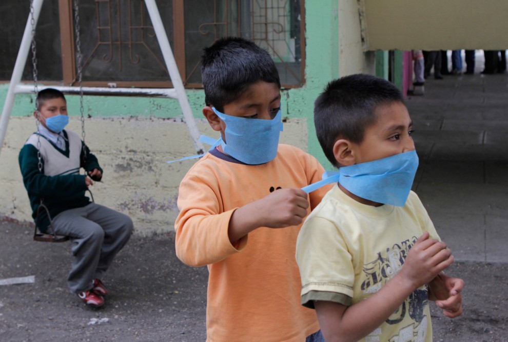 Мальчик помогает другу надеть защитную маску, предоставленную «Красным Крестом», в городе Сан Николас де Лос Ранчос, Мексика,17 апреля 2012 года. Занятия в местных школах были приостановлены из-за извержения вулкана Попокатепетль. 