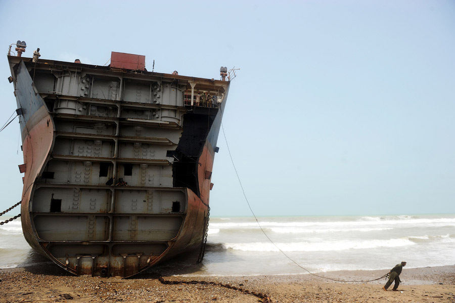 Рабочий тянет трос к силовому механизму для последующего удаления части обшивки судна, выброшенного на берег, Карачи, Пакистан,10 июля 2012 г.
