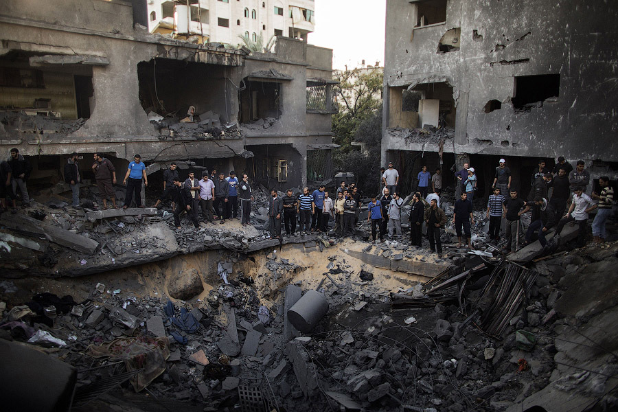 Палестинцы собрались вокруг воронки, образовавшейся после авиаудара израильских ВВС по дому семьи al-Dallu в Газе, 18 ноября 2012 года.