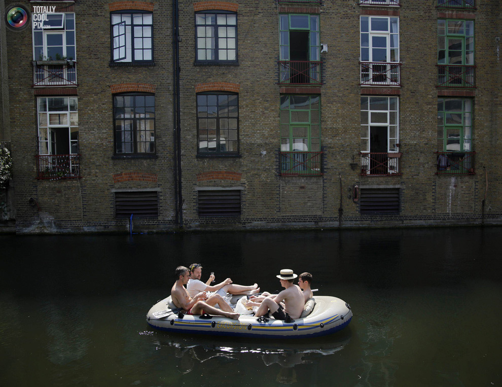 Мужчины плывут по Риджентс-каналу мимо облагороженного складского здания в Лондоне. 