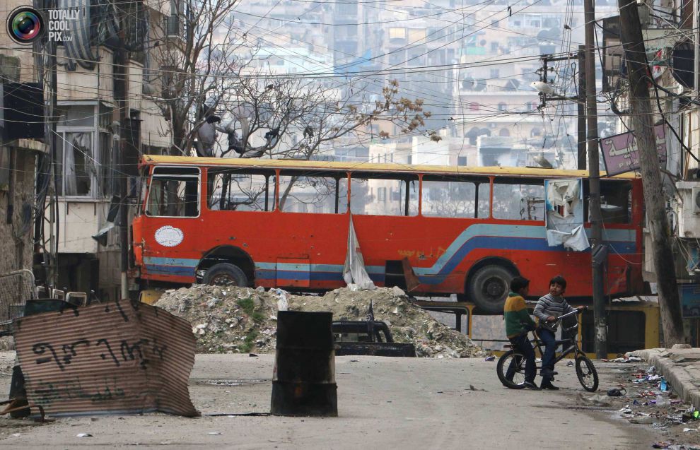 Дети играют возле автобуса, который заслоняет улицу от снайперского огня, в подконтрольном повстанцам районе Бустан аль-Кастр в Алеппо.