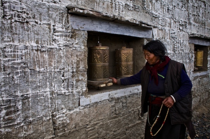 Старая тибетская женщина поворачивает цилиндры, которые сделаны из позолоченной бронзы и покрыты буддийскими надписями и символами, произнося мантру Ом Мани Падме Хум